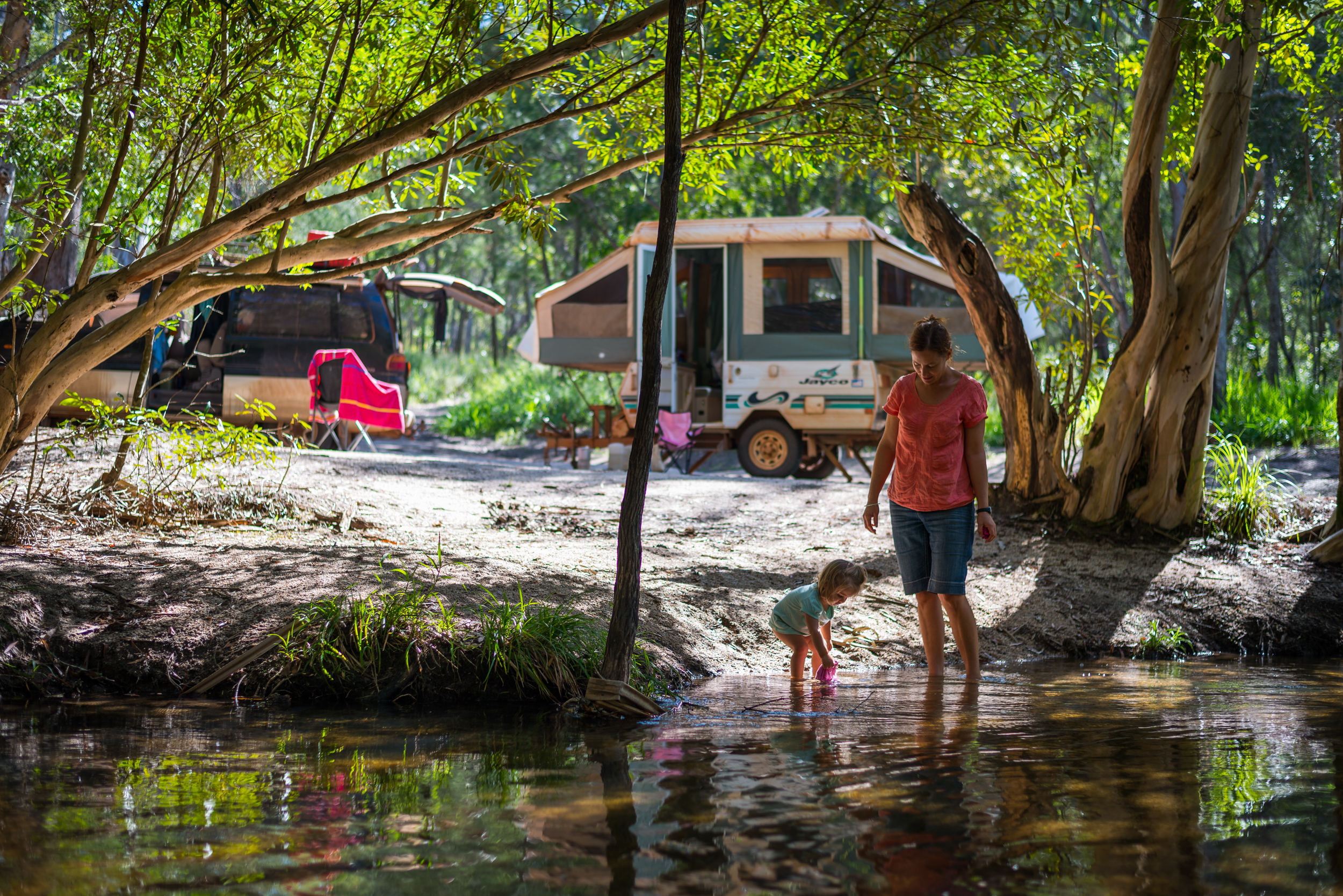 Girl playing in the water while her mum watches at a camping site