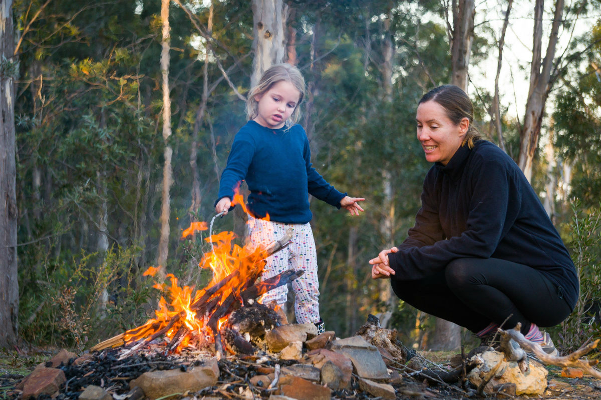 young girl poking a fire with her mum