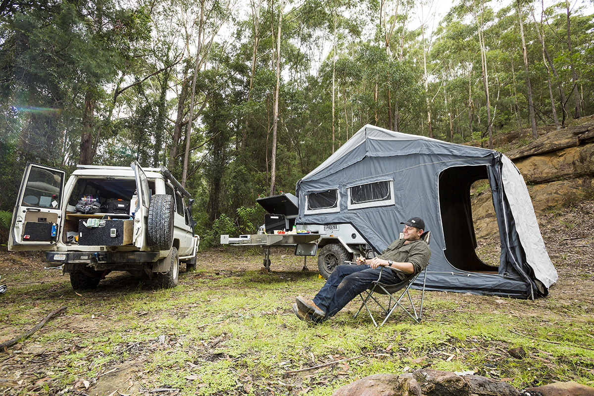 A-man-sitting-next-to-the-car-and-a-camper-trailer