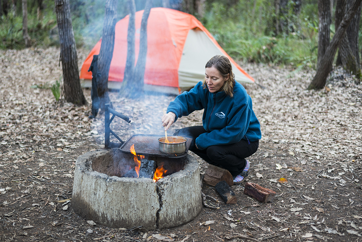 A woman is cooking on fire at the camp site