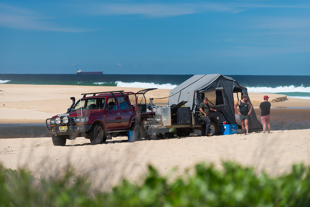 People-standing-around-a-camper-trailer-setup-and-a-car-on-the-beach