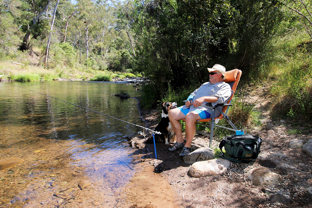 Man-sitting-on-the-campchair-next-to-the-lake-fishing